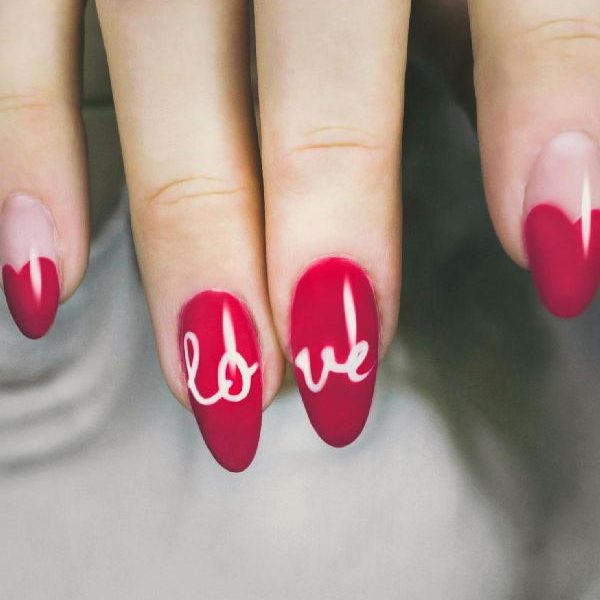 Uñas largas pintadas de rojo con diseño de corazón y la palabra "love" en color blanco, perfectas para una manicura romántica y elegante.